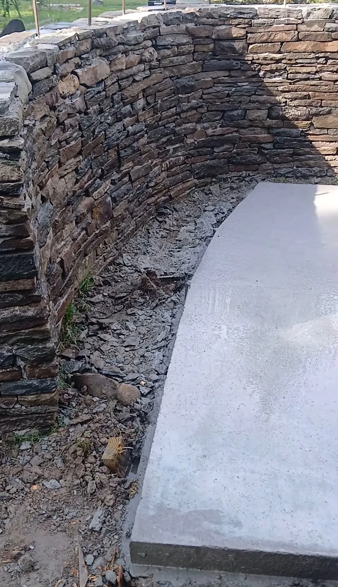 Curved dry-stacked stone wall around a fresh concrete pad